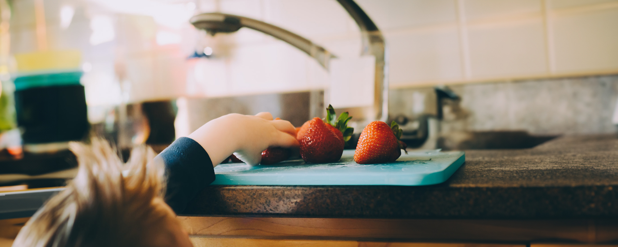 Small child reaches for strawberries on a kitchen counter